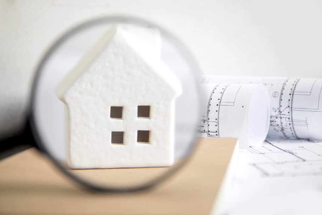 Maison miniature examinée avec une loupe symbolisant l'état des lieux d'un logement à Caen.
