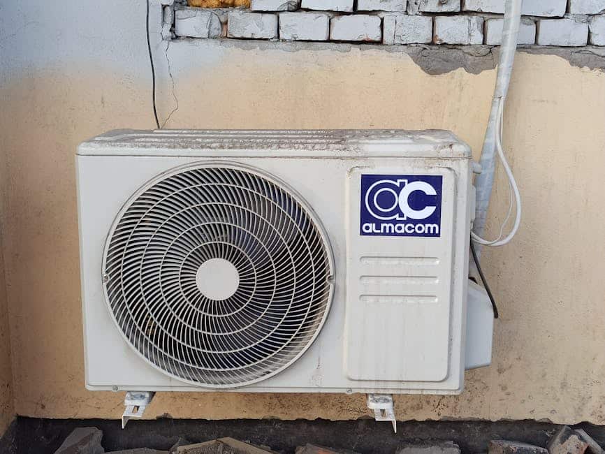 Unité extérieure de climatisation murale avec ventilateur, tuyauterie et câblage visibles sur façade