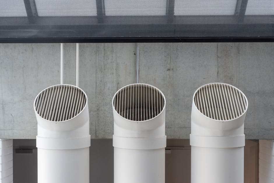 Trois conduits de ventilation circulaires blancs avec grilles d'extraction inclinées dans un intérieur industriel